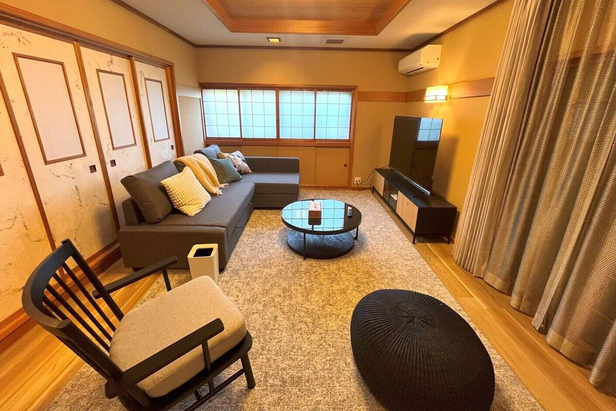 A living room with a sofa, a round coffee table, a TV, and a window with curtains.