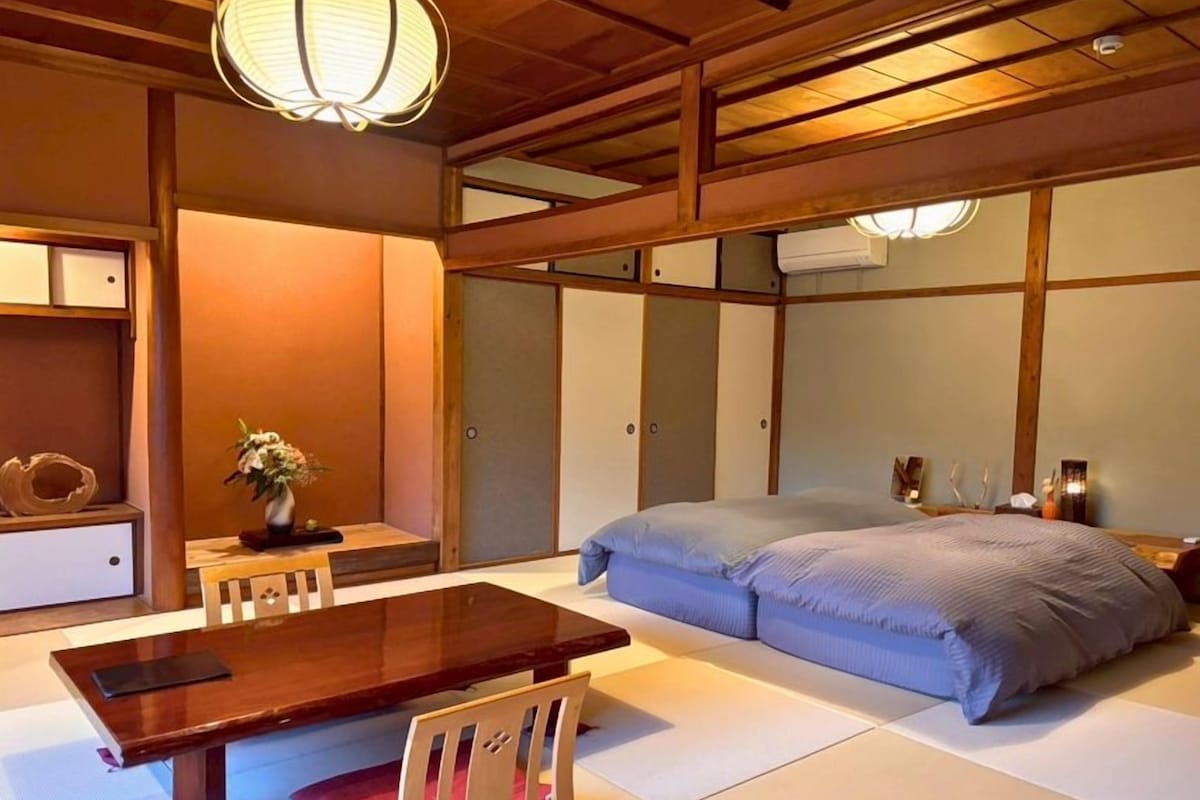 A traditional Japanese-style room with tatami flooring, a low wooden table, a bed with blue bedding, and a hanging paper lantern.