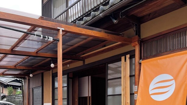Un edificio japonés tradicional con fachada de madera, un porche cubierto y un gran cartel naranja con caracteres japoneses.