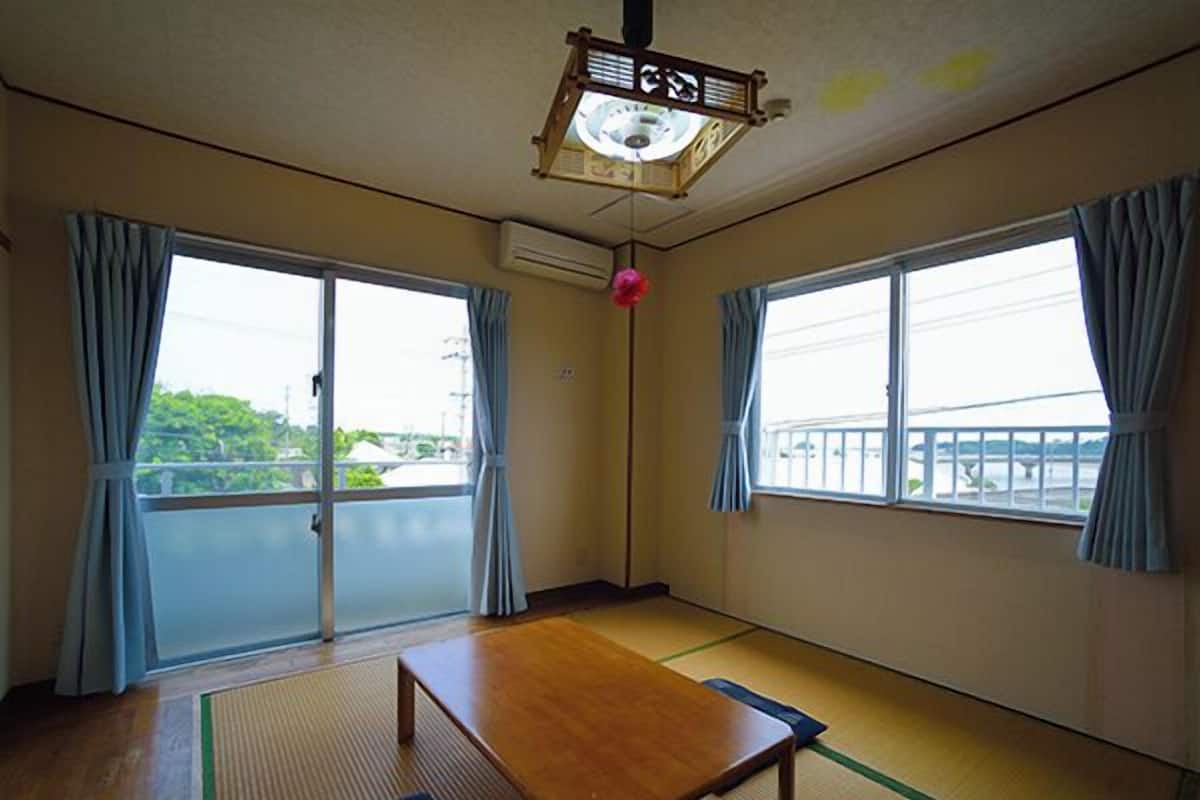 A room with tatami flooring, a wooden table, and two windows with curtains.