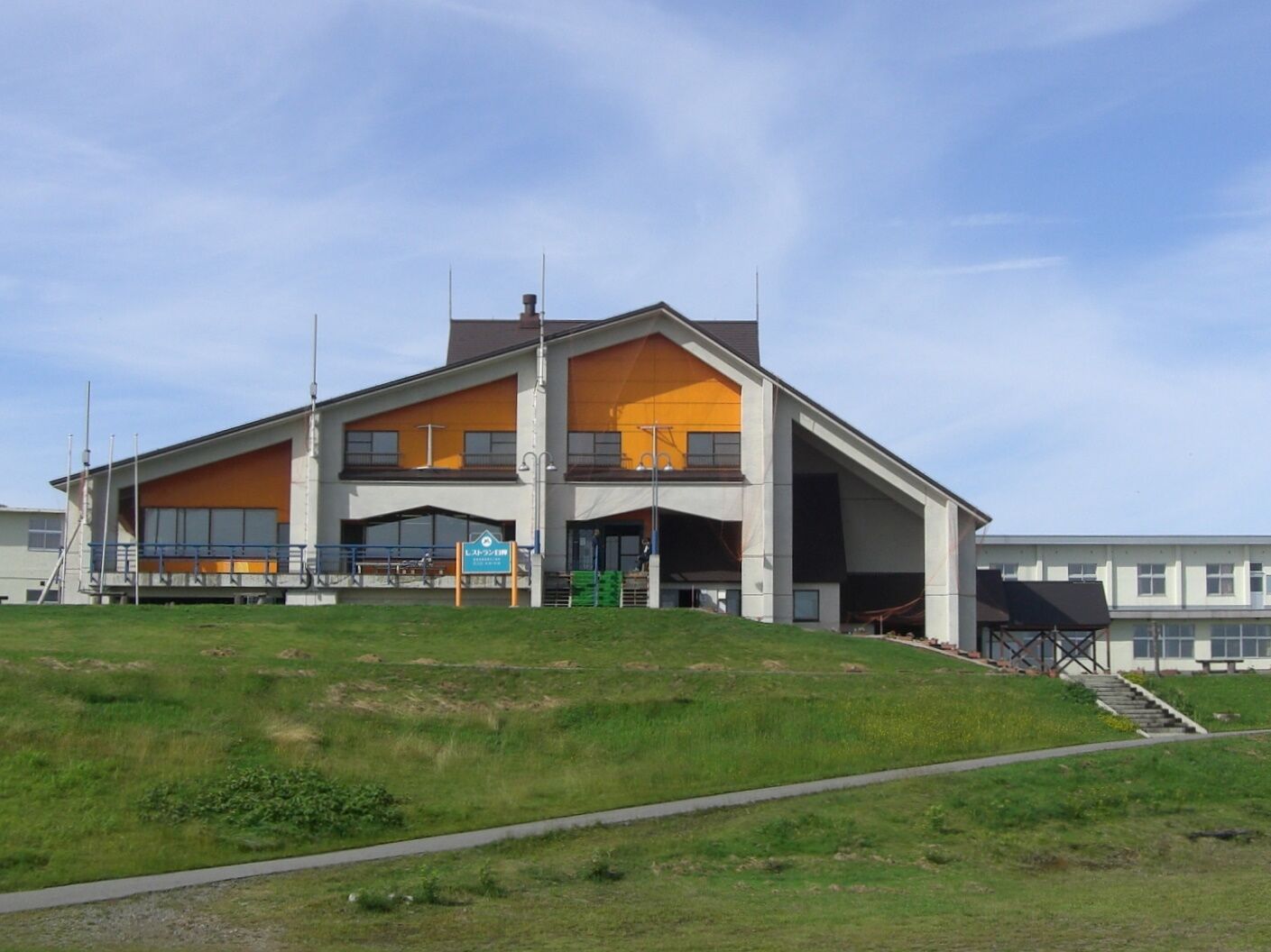 Un bâtiment moderne doté d’un toit plat, de grandes fenêtres et d’une colline verdoyante au premier plan.