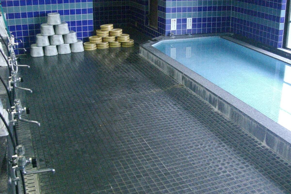 A pool area with tiled walls, a pool, and a row of faucets on the left.