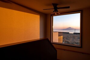 Quarto com uma janela ampla, um ventilador de teto e vista para uma paisagem distante.