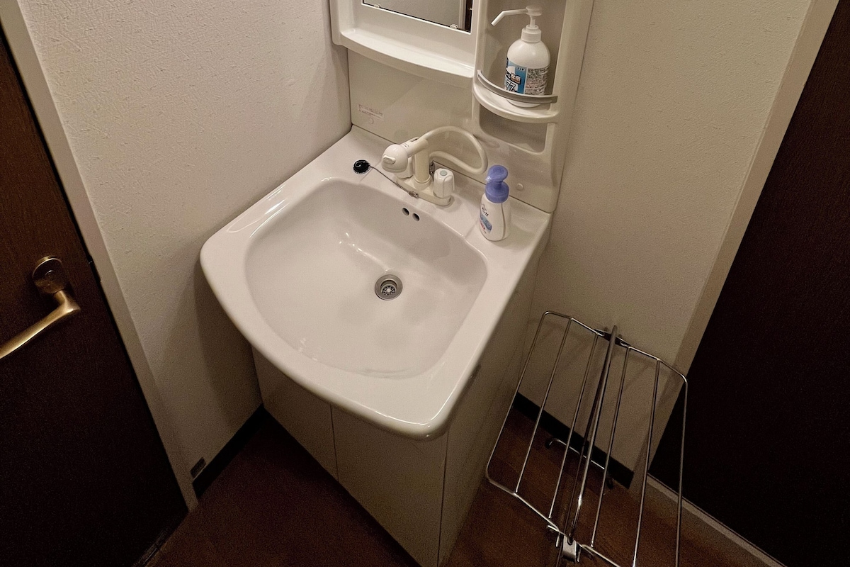 Une salle de bain équipée d’un lavabo, d’un miroir, d’un distributeur de savon et d’une étagère contenant des articles de toilette.