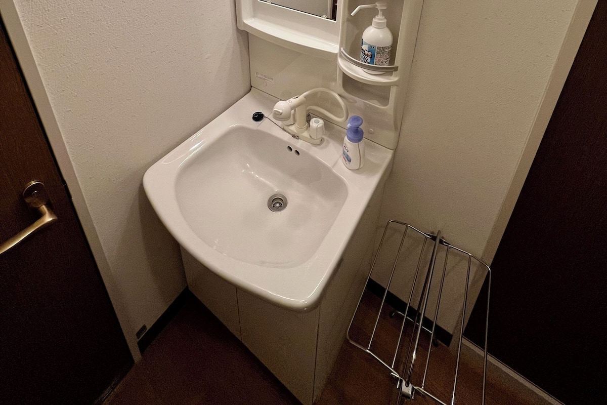 A bathroom with a sink, mirror, soap dispenser, and a shelf with toiletries.