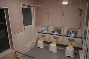 Baño público con tres inodoros, una ventana y estantes con artículos de aseo.