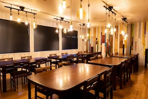 Un comedor con mesas y sillas de madera, lámparas colgantes y una pared colorida.