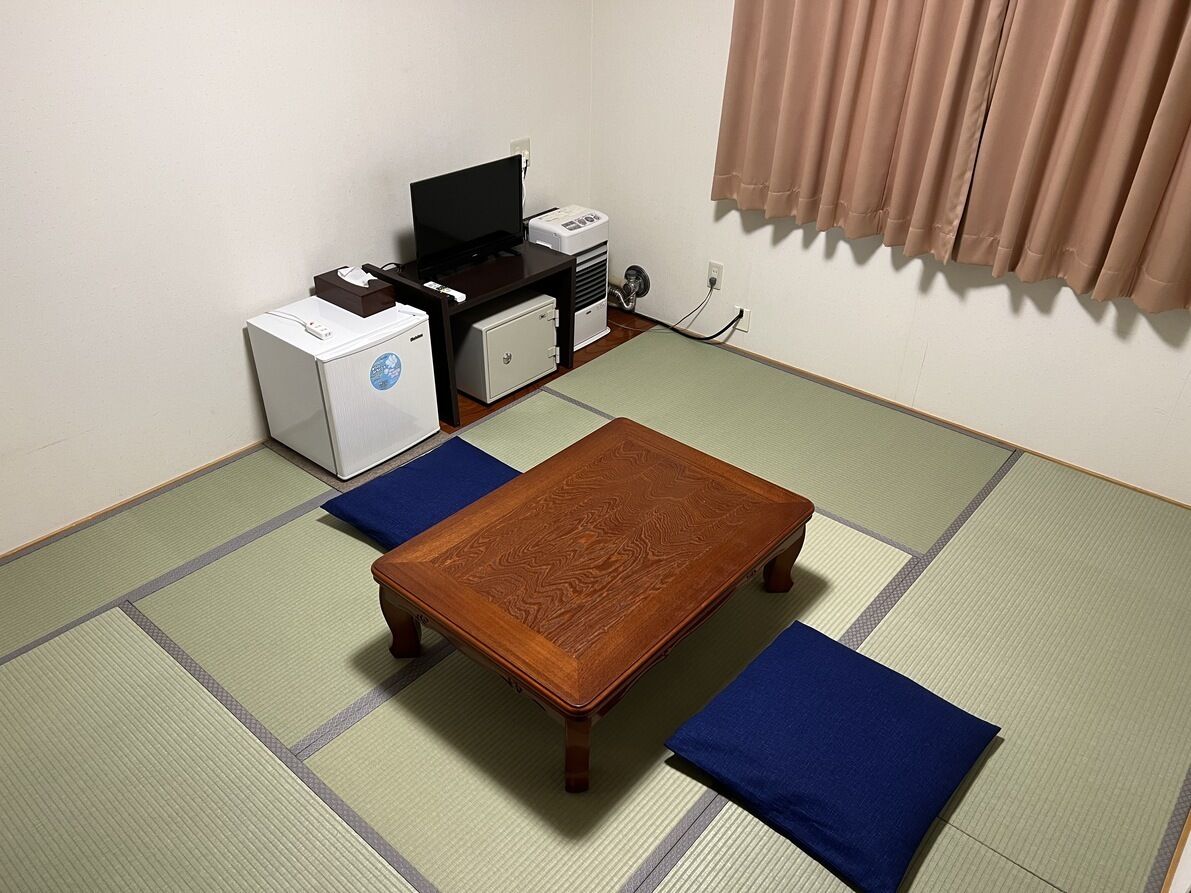 Quarto com piso de tatame, mesa de madeira, almofadas azuis, televisão e impressora.