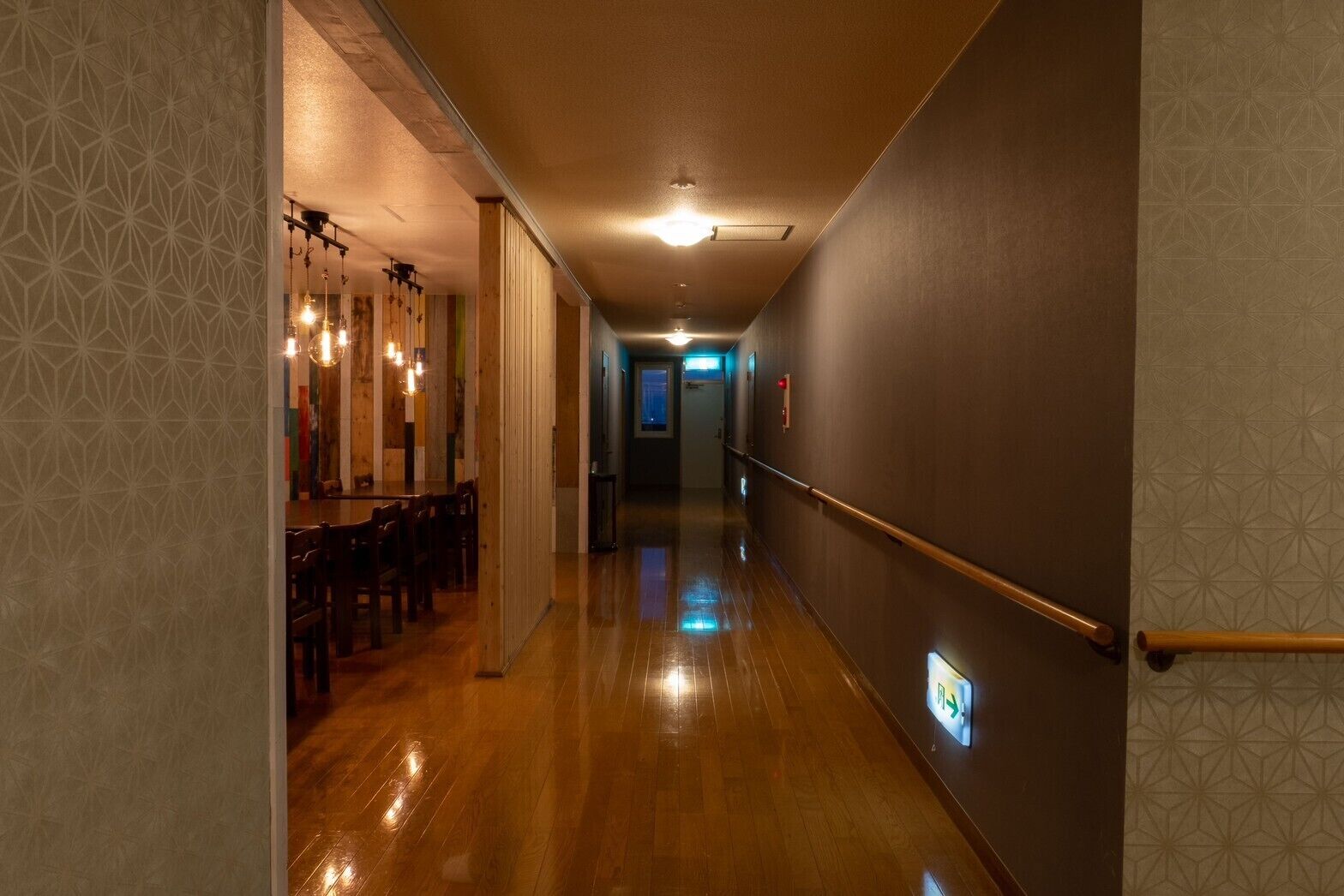 A hallway with wooden flooring, a dining area with hanging lights, and a wall-mounted handrail.