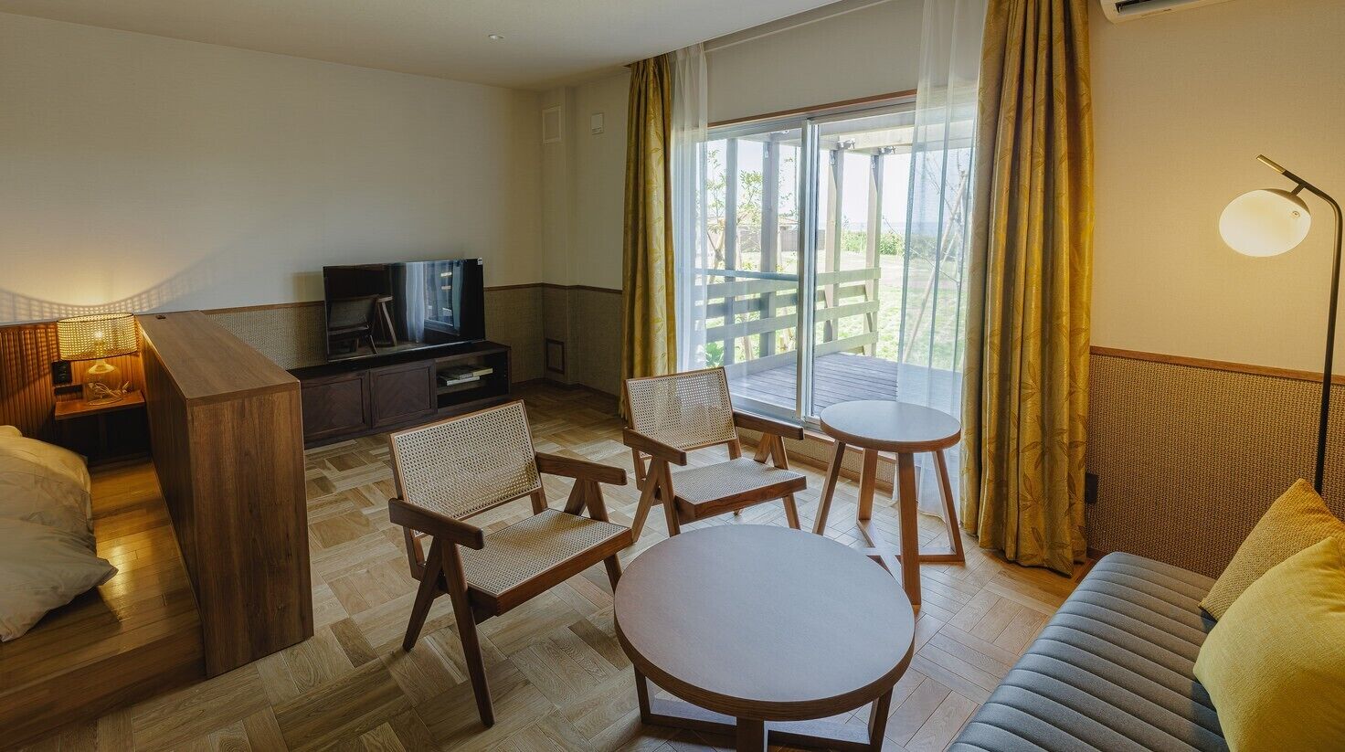 Ein Hotelzimmer mit einer Couch, einem runden Tisch, zwei Stühlen, einem Fernseher und einem Balkon mit Vorhängen.