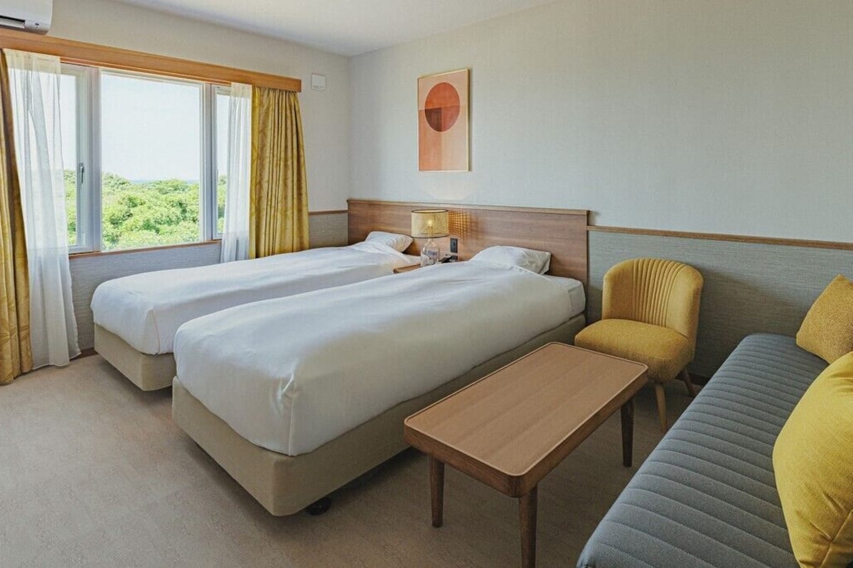 Quarto de hotel com duas camas, um sofá, uma mesinha e uma janela com cortinas.