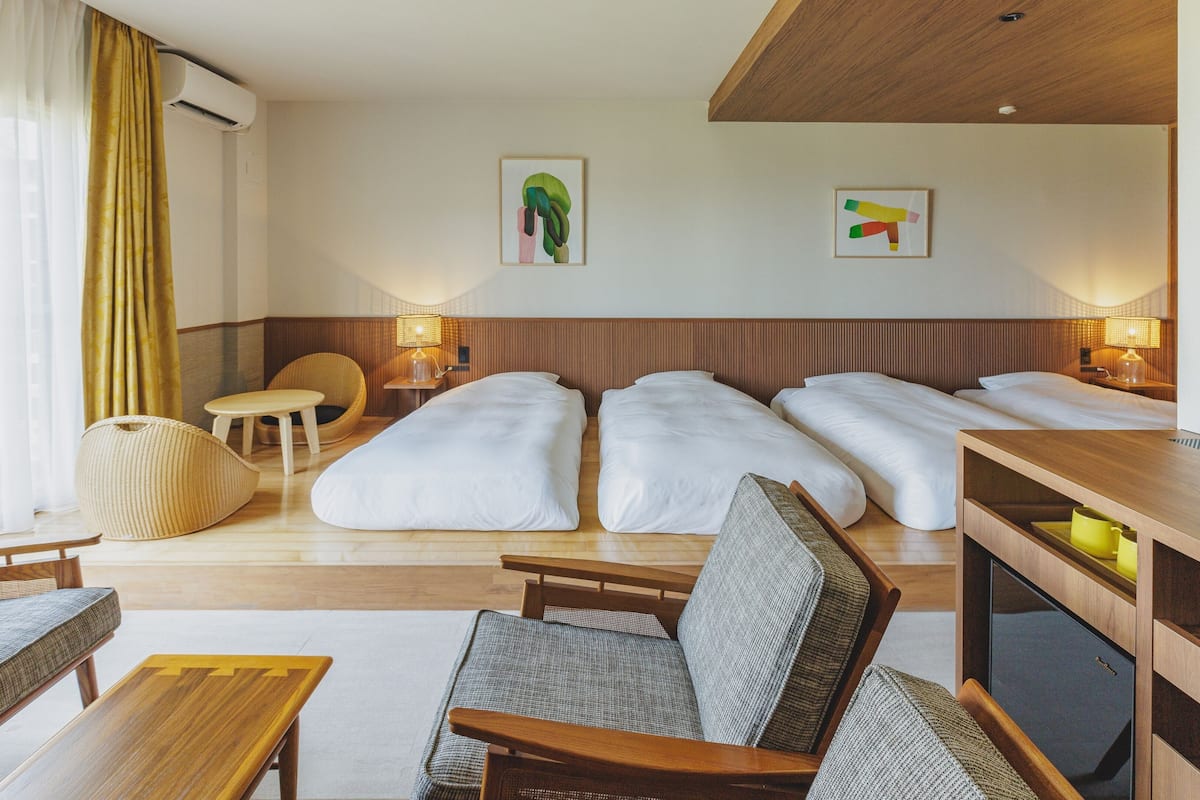 Quarto de hotel com cama, duas mesas de cabeceira, uma cadeira, uma mesinha e um sofá.
