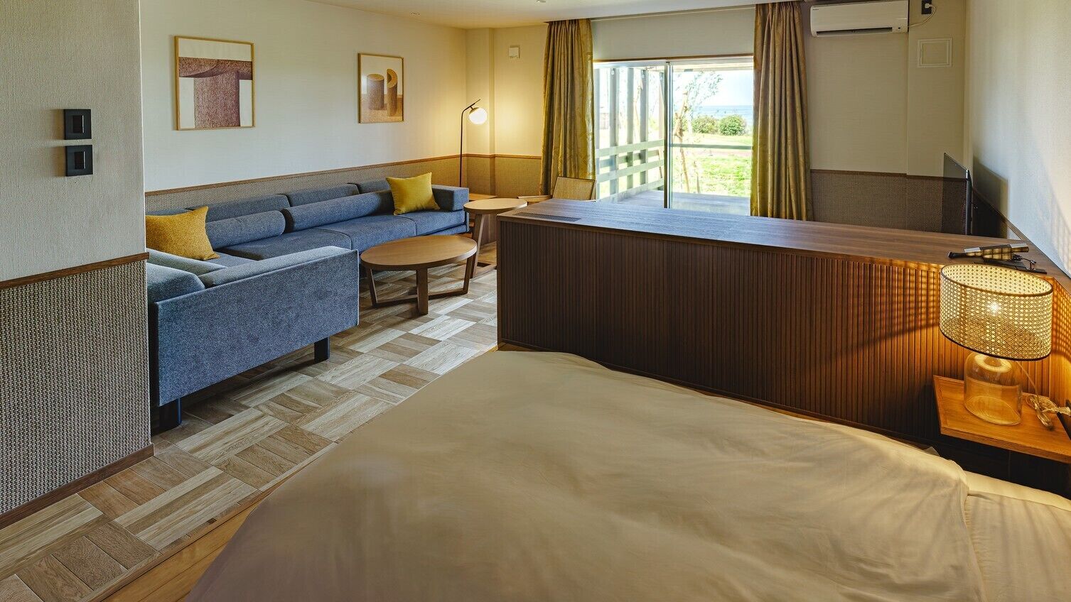 A hotel room with a bed, a sofa, a small table, a desk, and a view of the outdoors.