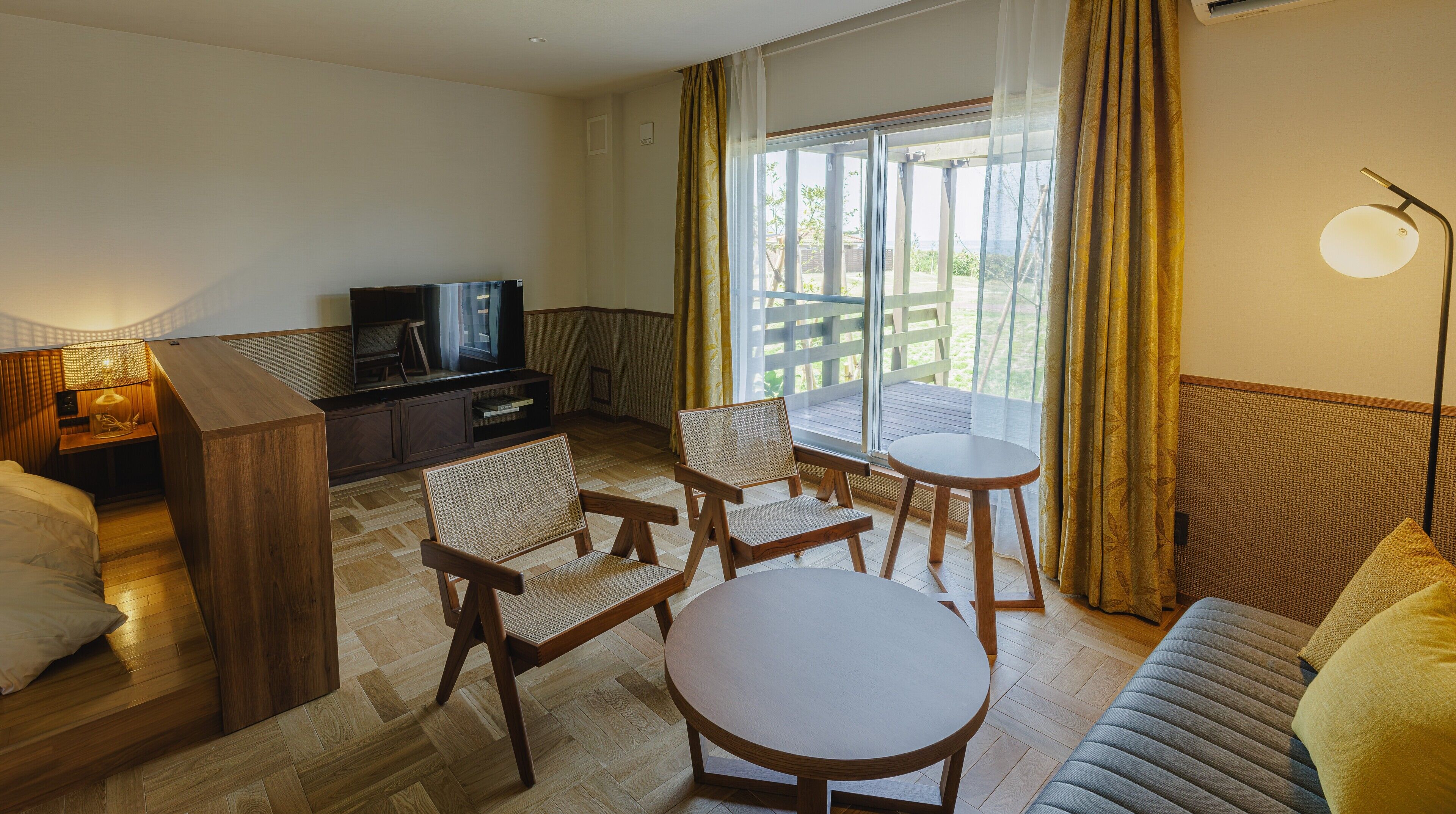 A hotel room with a TV, wooden furniture, a balcony with a view, and a lamp.
