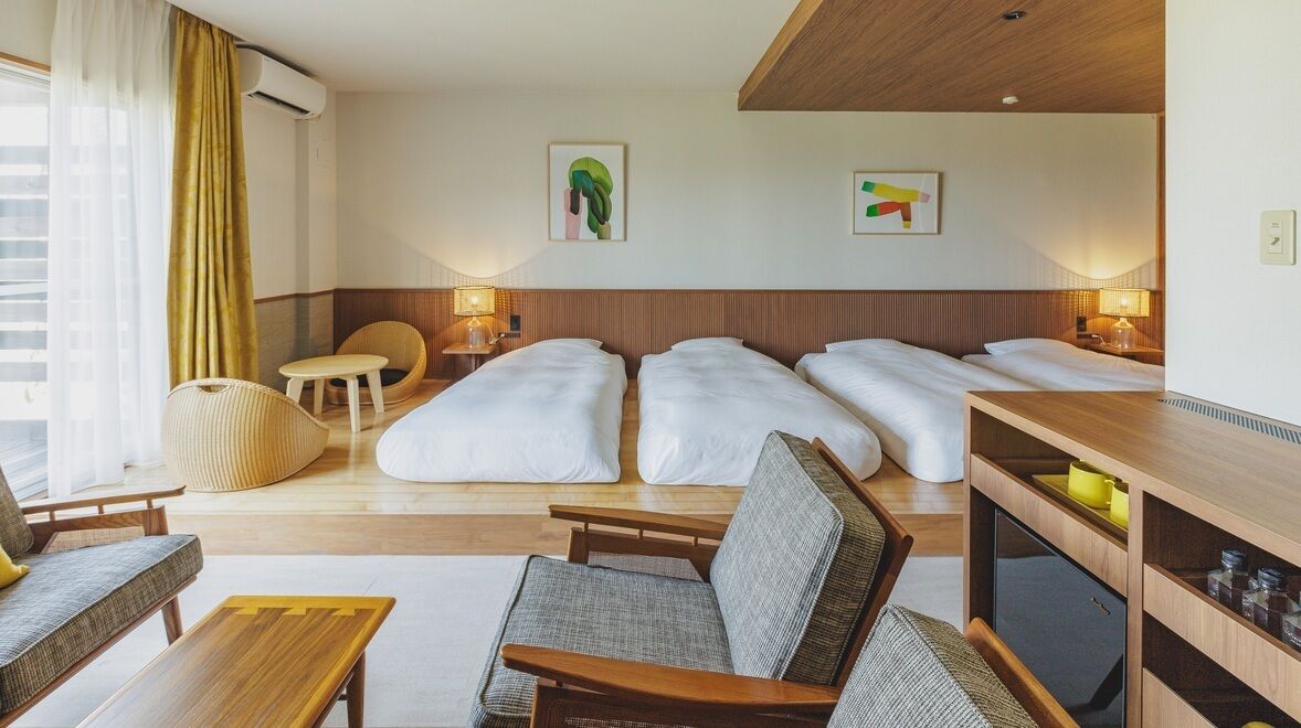 Ein Hotelzimmer mit einer Couch, zwei Einzelbetten, einem kleinen Tisch, einem Sessel und einem Fernseher.