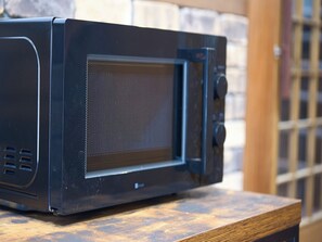 A black microwave oven on a wooden surface with a brick wall in the background. - Tabihaku Stay Kasumi (Kami)