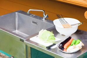 A stainless steel kitchen sink with a faucet, a cutting board with a knife, a bowl with whisk, and a plate with vegetables. - Tabihaku Stay Kasumi (Kami)