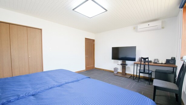 A hotel room with a bed, a desk with a chair, a television, and an air conditioning unit. - Tabihaku Stay Kasumi (Kami)