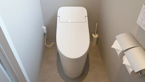 Ein kleines Badezimmer mit Toilette, sichtbarer Steckdose und einer Toilettenpapierrolle an der Wand.