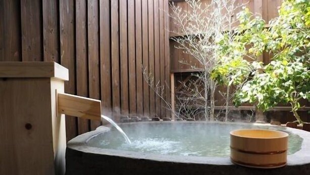 Un bain thermal en plein air, avec un banc en bois, entouré de murs en bois et de plantes en pot.
