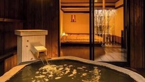 Un onsen japonais traditionnel, avec un bain en bois, une structure en bois dotée d’un bec verseur, et une vue sur une pièce comprenant un lit et un mur en bois.