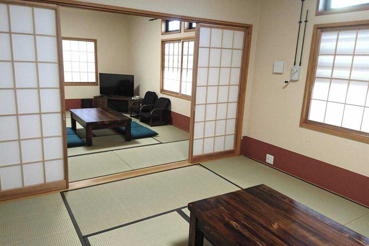 Una habitación japonesa tradicional con suelo de tatami, un televisor, un sofá y puertas correderas.