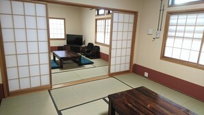 Une pièce de style japonais traditionnel, avec un sol recouvert de tatamis, une télévision, un canapé et des portes coulissantes.
