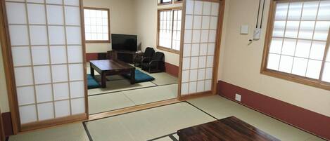 A traditional Japanese room with tatami flooring, a television, a sofa, and sliding doors.