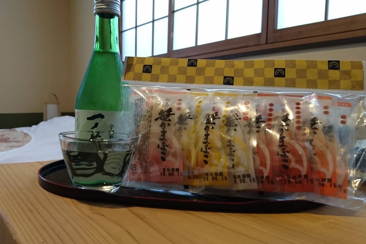 Una botella de líquido verde, un vaso y una bandeja con productos envasados sobre una superficie de madera.