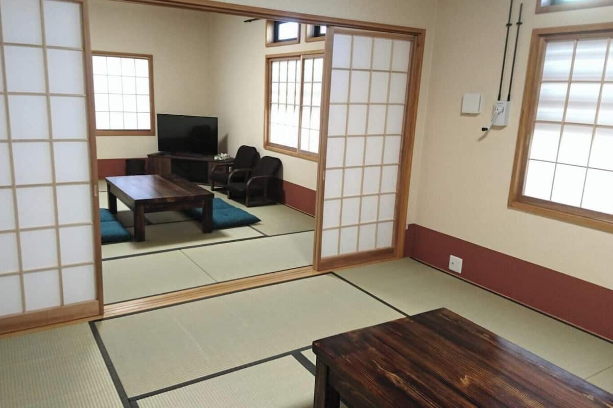 Una habitación tradicional japonesa con suelo de tatami, una mesa baja, un sofá y puertas correderas.