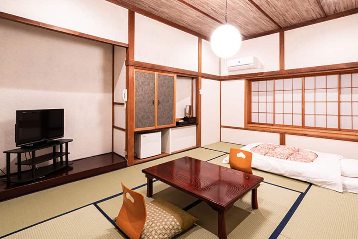 Ein traditioneller japanischer Raum mit Tatami-Böden, einem Fernseher, einer Couch und einem Holztisch.