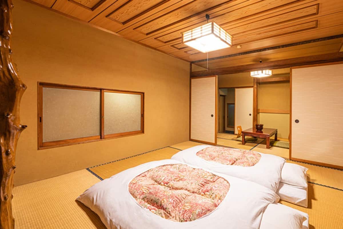 Ein traditioneller japanischer Raum mit Tatami-Boden, zwei Tatami-Betten mit floralen Bettdecken, einer Holzzieldecke und Schiebetüren.
