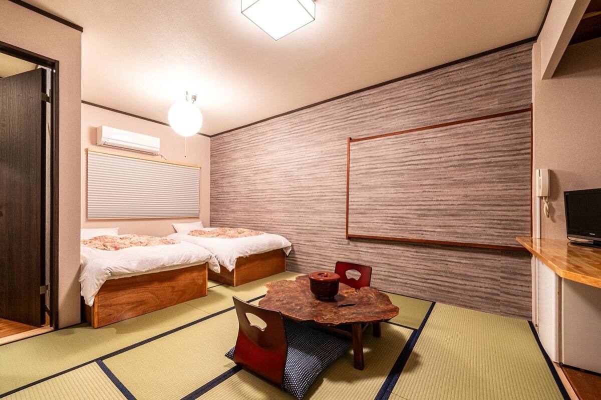 Ein Zimmer mit zwei Betten, einem kleinen Tisch, einem Fernseher und einem Badezimmer.