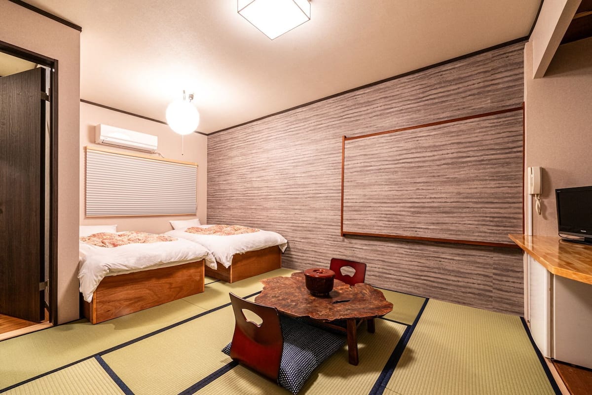 Quarto com duas camas, uma mesinha, televisão e banheiro.