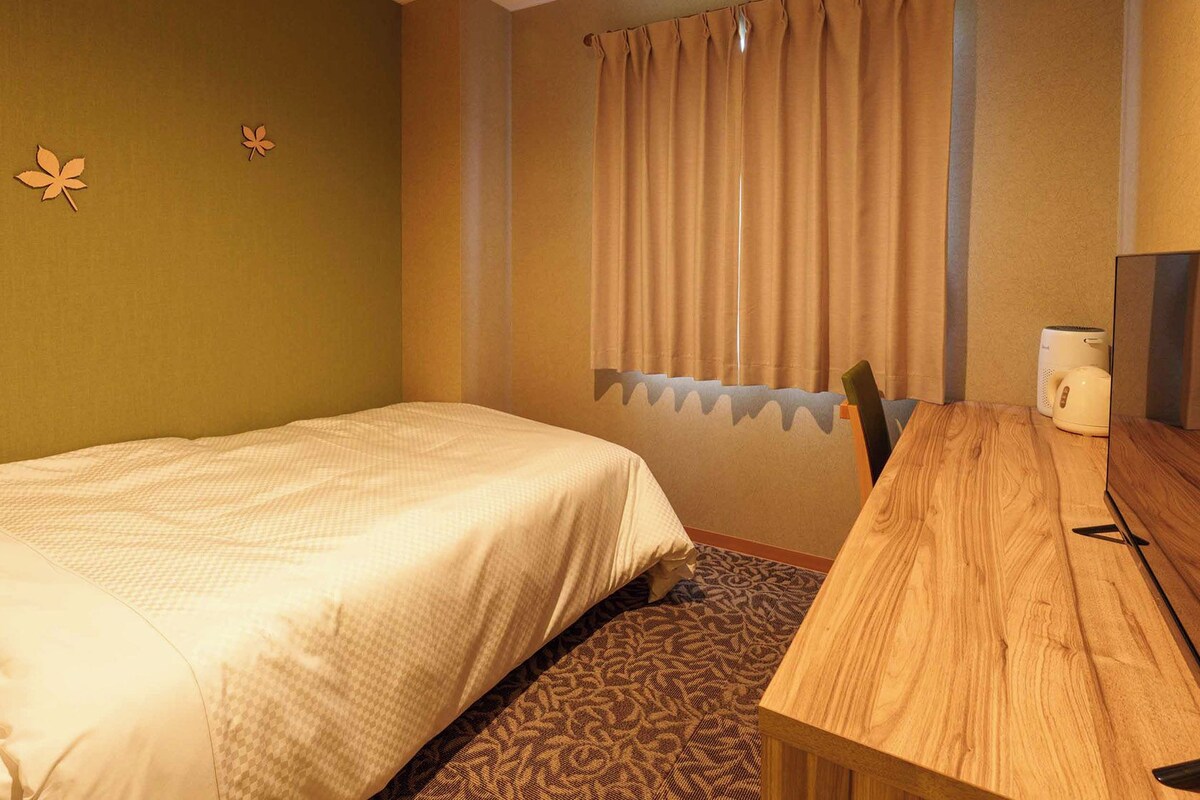 Habitación de hotel con cama, escritorio de madera, televisor y ventana con cortinas.