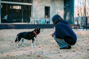 A person crouching on a grassy area with a dog, a building with large windows and a door in the background. - Ash Villa Fujikawaguchiko (Narusawa)