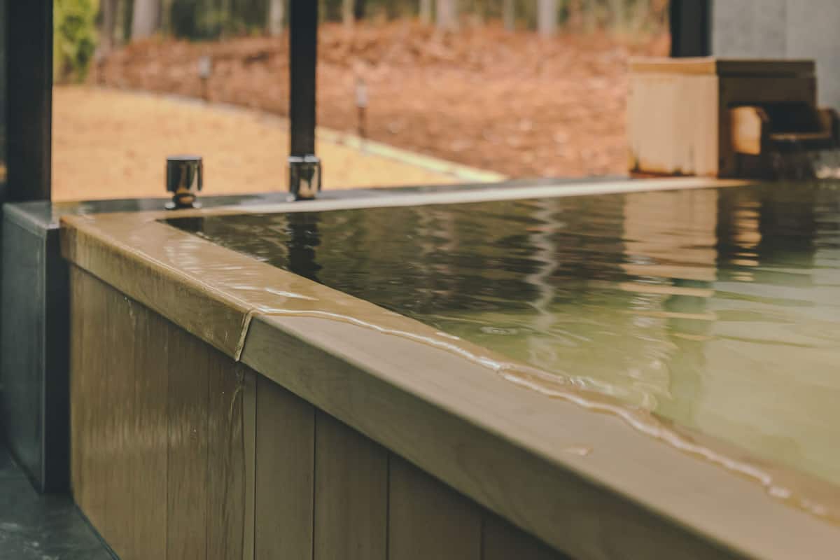 A wooden spa tub with a view of a garden.