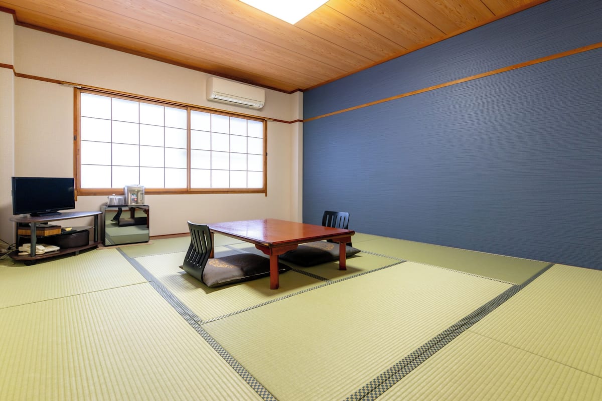 A traditional Japanese room with tatami flooring, a wooden table, a television, and a sliding door.