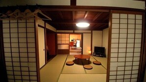 A traditional Japanese room with tatami flooring, a tatami mat table, a television, and sliding doors.