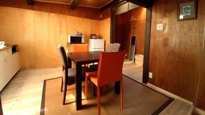 A wooden interior with a dining table, chairs, a microwave, and a refrigerator.
