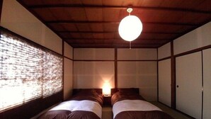 A traditional Japanese-style room with tatami flooring, two beds with dark bedding, a hanging light fixture, and sliding doors.