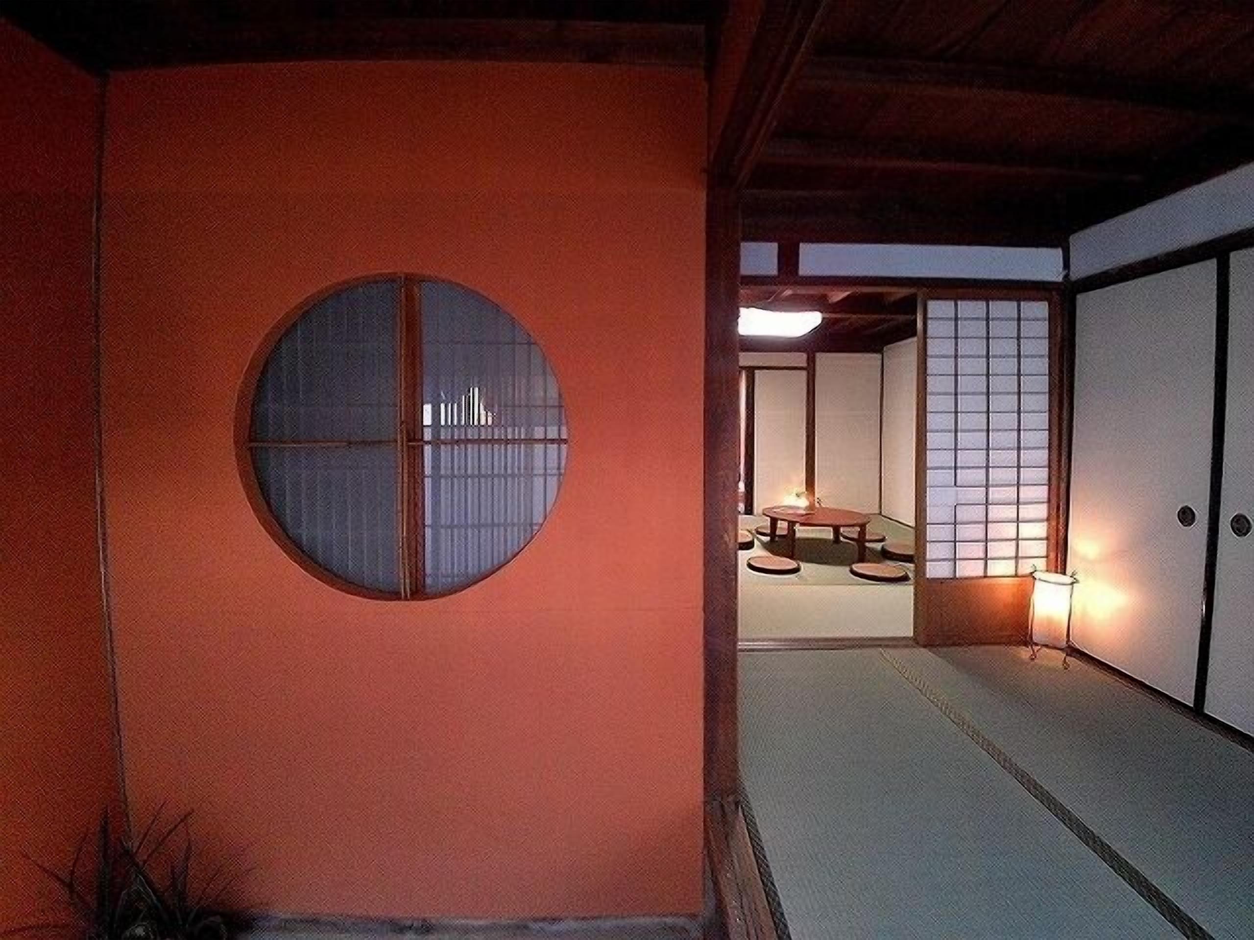 Una habitación japonesa tradicional con suelo de tatami, un panel de fusuma y un ventanal circular.