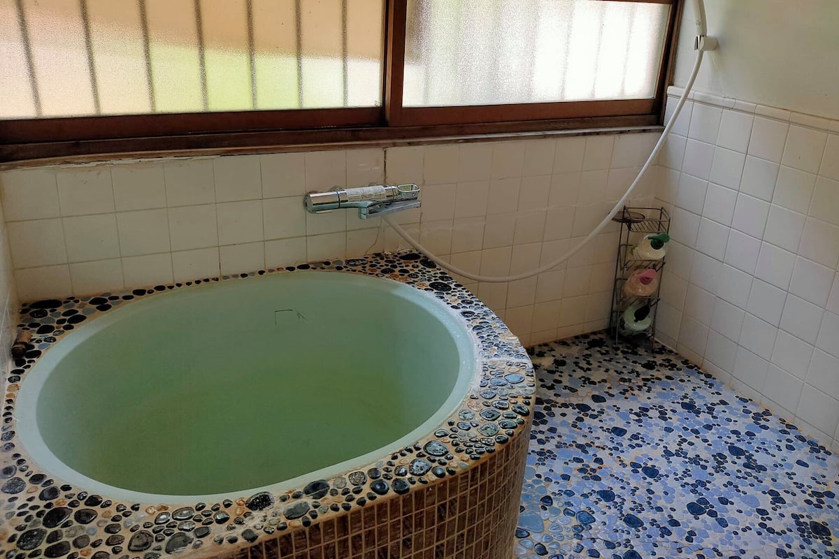 Un baño con una bañera independiente, una ventana con marco de madera y un suelo de baldosas con diseño de guijarros.