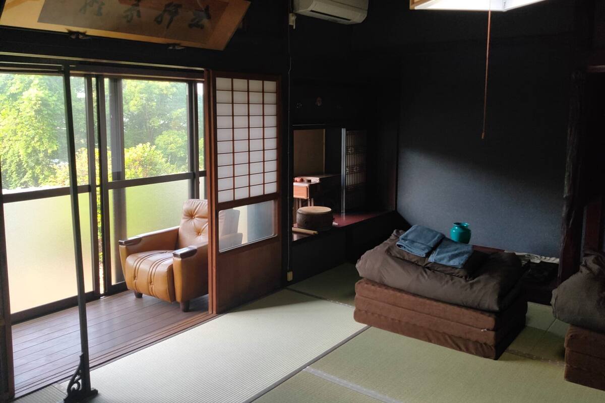 Una habitación japonesa tradicional con suelo de tatami, un panel corredizo shoji, una zona de estar con cojines y un televisor.