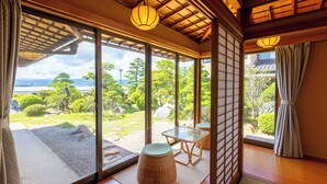 Una habitación con grandes puertas de vidrio correderas, suelo de esteras de tatami, una mesa baja con cojín y un farolillo tradicional.