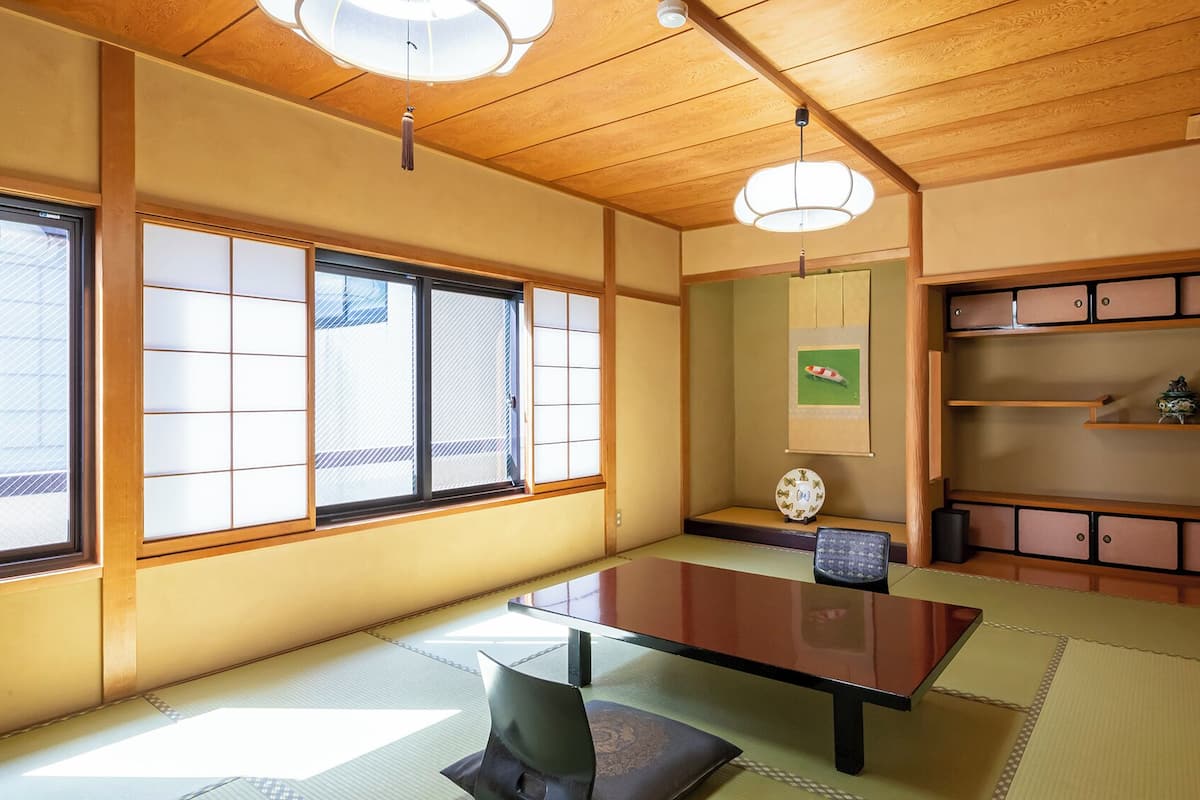 Una habitación tradicional japonesa con suelo de tatami, una mesa baja, puertas correderas y una estantería con adornos decorativos.