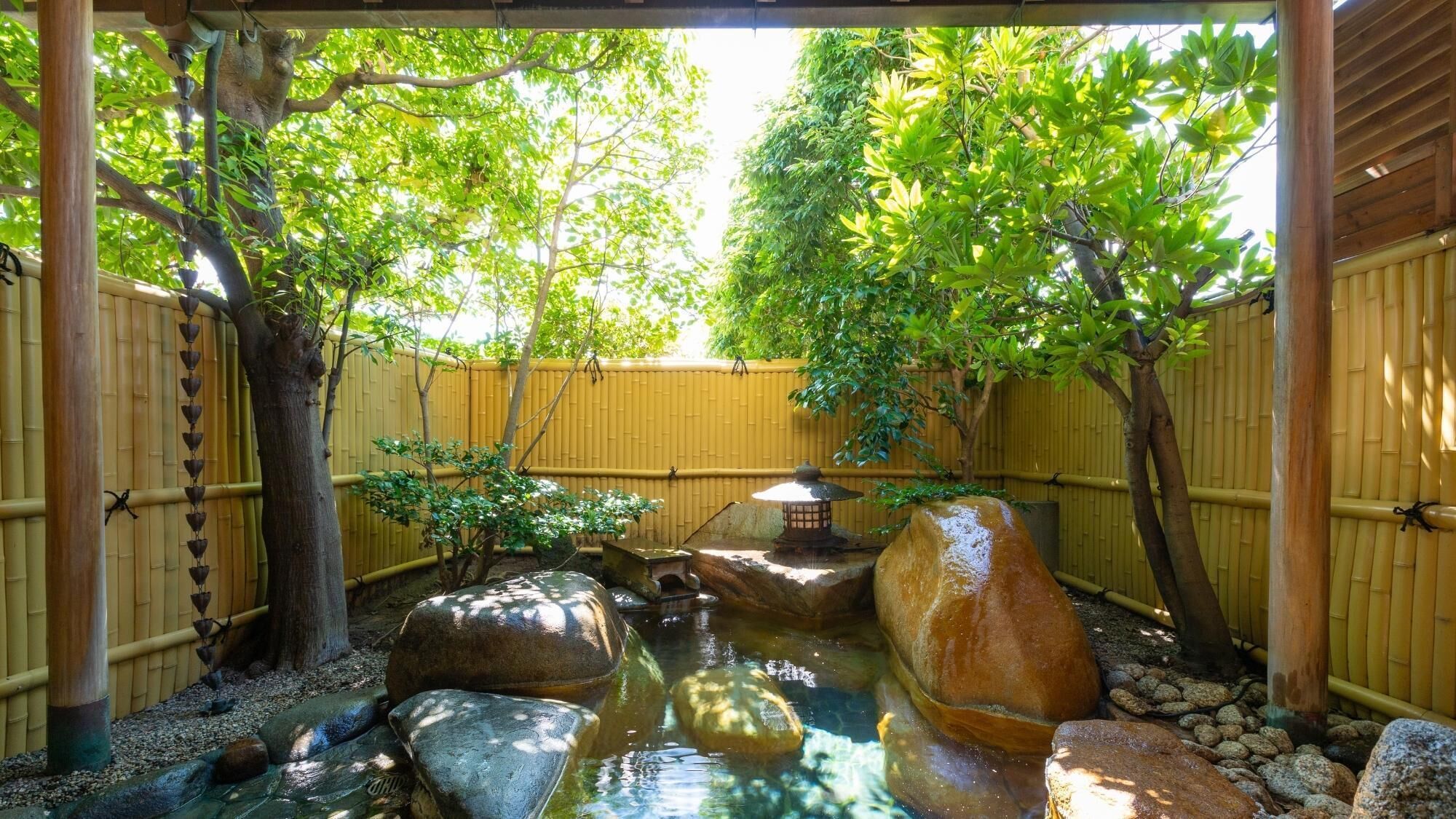 Um jardim tranquilo com um elemento de água, cerca de bambu e um tradicional lampião japonês.