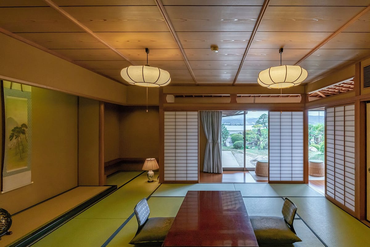A traditional Japanese room with tatami flooring, shoji screens, and a low table with cushions.