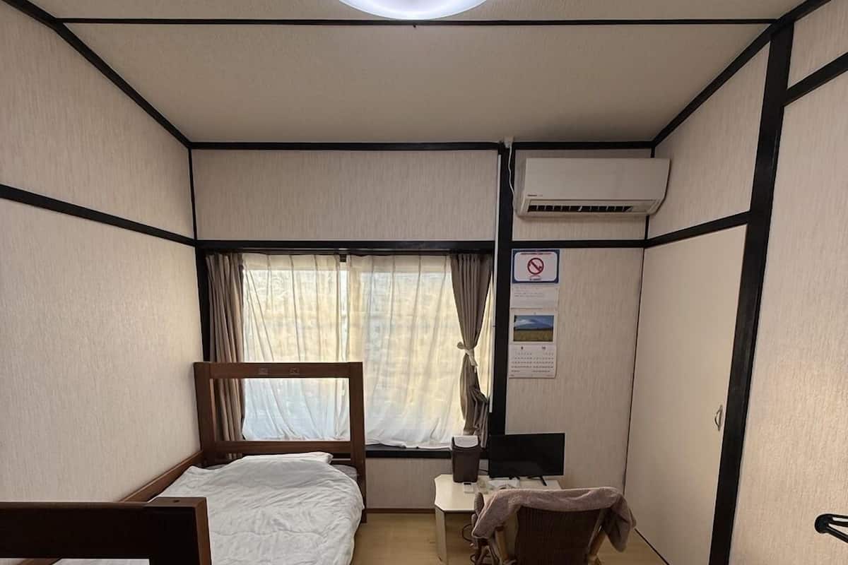 Habitación de hotel compacta con una cama individual, un escritorio, una silla y un equipo de aire acondicionado.