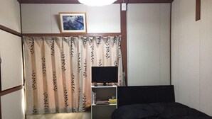 A bedroom with a bed, a TV on a stand, a bookshelf, and a curtain with a leaf pattern. - Minshuku Warakuya (Kobayashi)